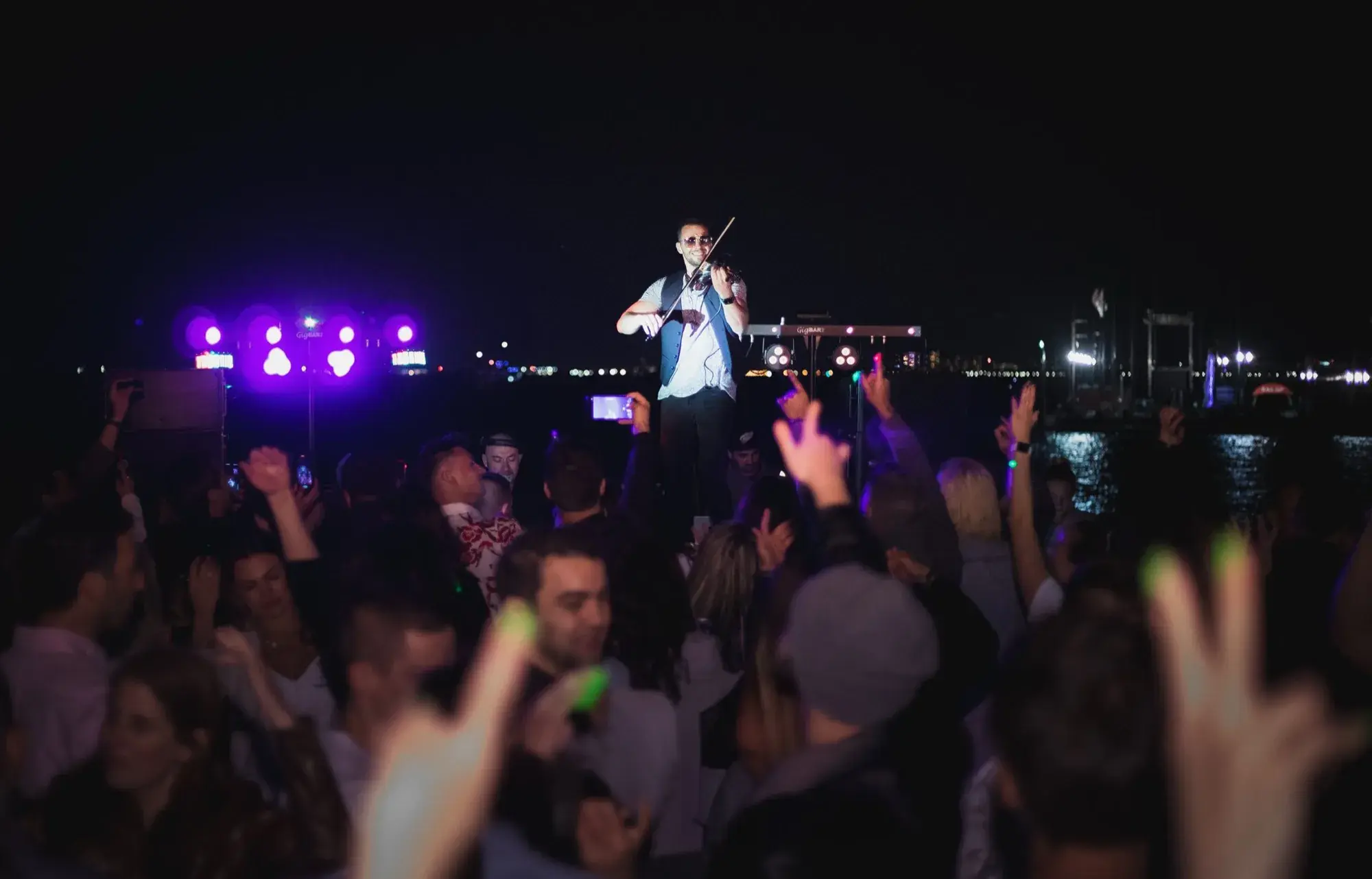 Live electric violinist playing over a packed dance floor at night on the water